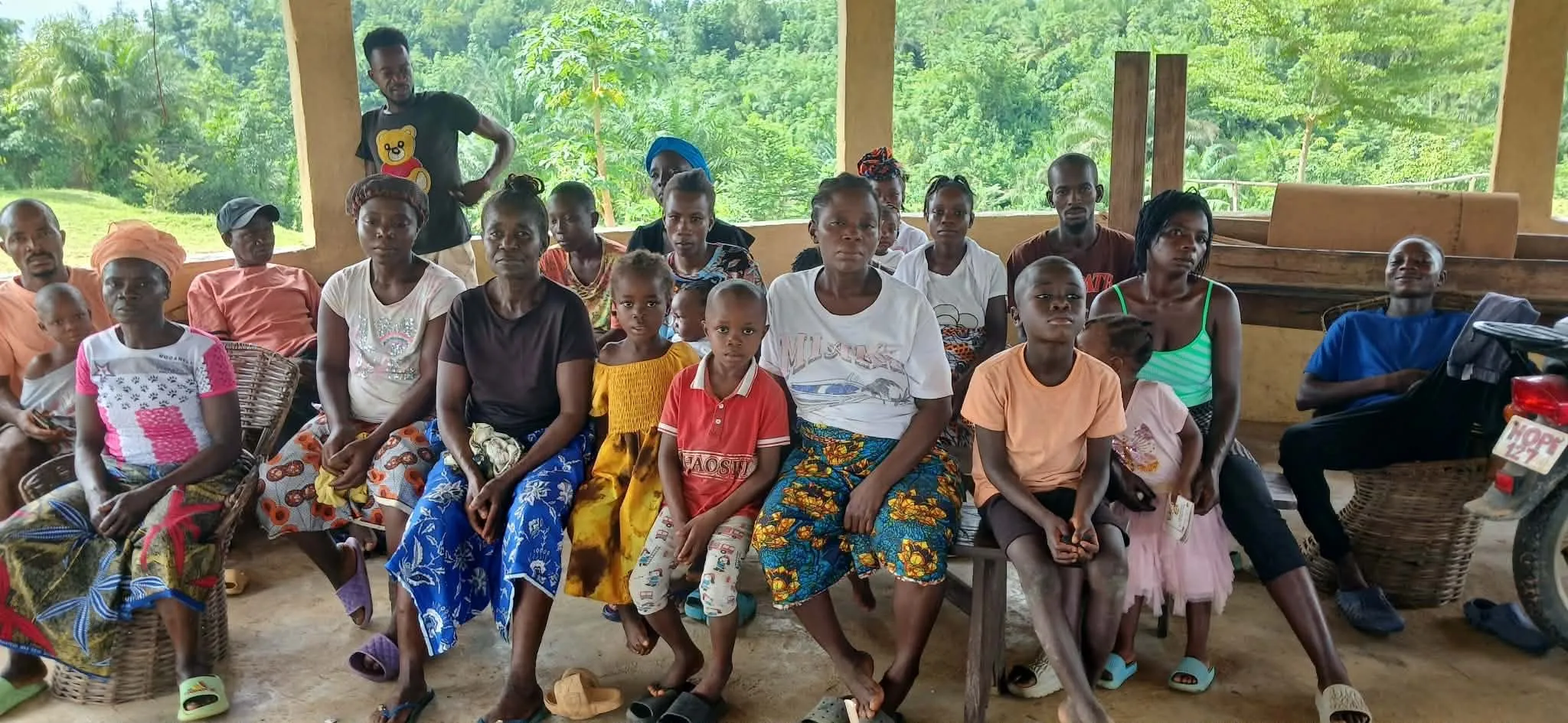 About twenty women and children seated on benches under an open-air shelter, waiting for care.